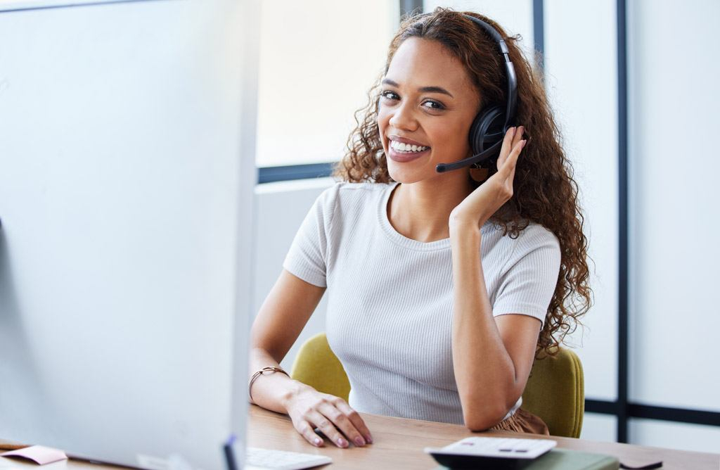 A friendly woman wearing a headset and talking on the phone with a customer.